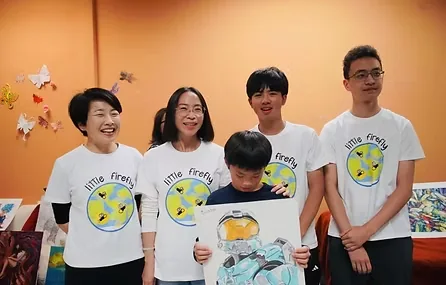 Little Firefly volunteers with a young artist holding artwork at an art fundraiser