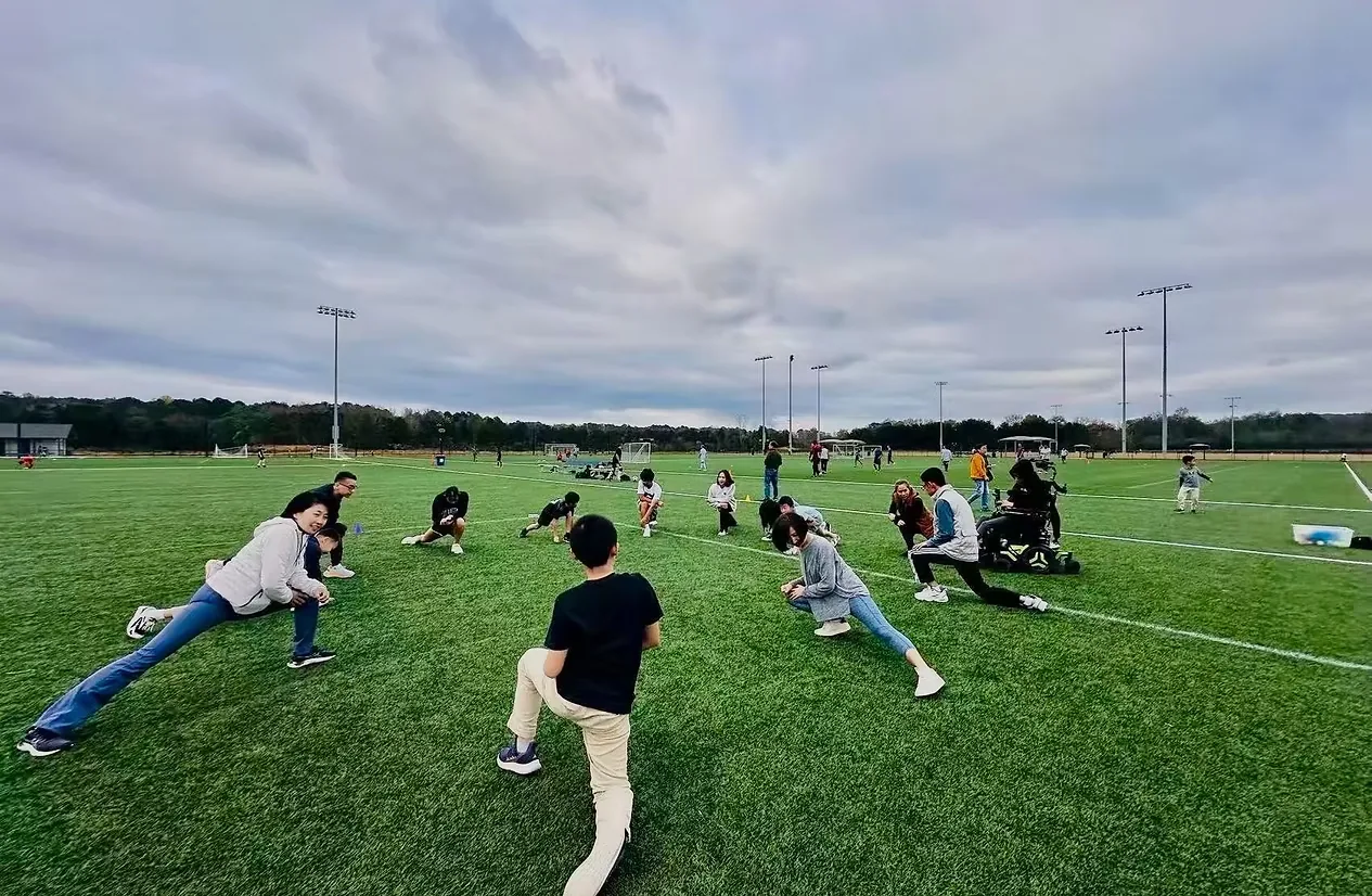 Little Firefly participants and volunteers stretching together on an outdoor field