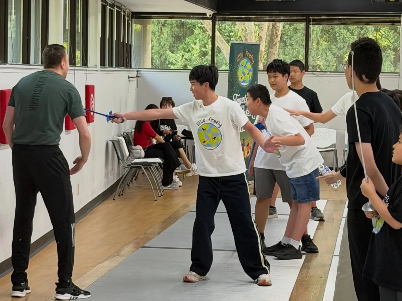 A Little Firefly participant practicing fencing with a coach and volunteers nearby